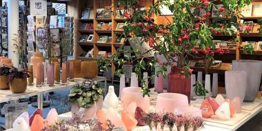 Lentecollectie glaswerk Dutz in roze en witte tinten in de cadeau- en boekenshop van Arboretum Kalmthout, presentatie op vierkante witte rekken, boeken en wenskaarten op de achtergrond.