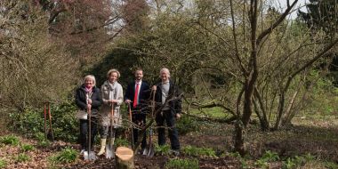 Twee vrouwen en twee mannen poseren met schup in de hand bij een boom die ze net gepland hebben in de tuin van Arboretum Kalmthout, plechtige boomplanting op een zonnige lentedag.