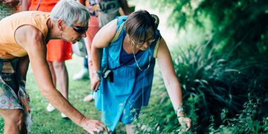 Twee vrouwen buigen voorover en voelen aan enkele planten in de groene borders van Arboretum Kalmthout, rondleiding door een gids tijdens de zomerse kookworkshop Bloemen op je bord.